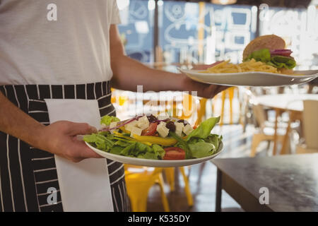 Mid section of waiter serving salade et frites avec burger dans cafe Banque D'Images