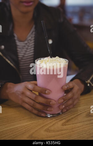 Mid section of woman avec verre à milkshake au café de table en bois Banque D'Images