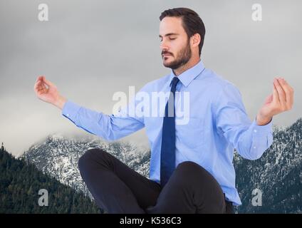 Digital composite of business man meditating contre les montagnes et ciel gris Banque D'Images