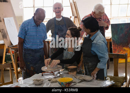 Happy friends looking at enseignant qui se pot en argile sur les poteries roue dans la classe d'art Banque D'Images