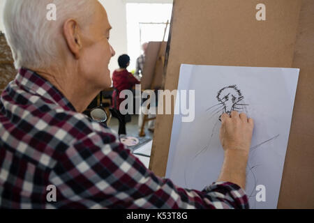 Vue latérale du senior homme esquisse sur papier dans la classe d'art Banque D'Images