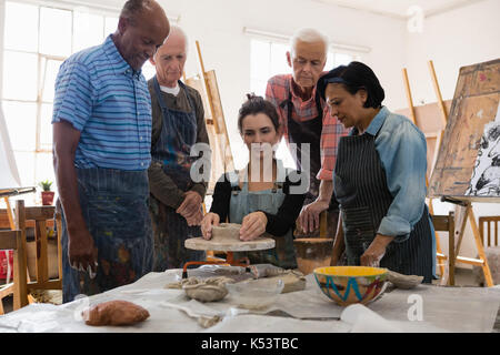 Senior friends à la recherche à l'enseignant qui se pot en argile sur les poteries roue dans la classe d'art Banque D'Images