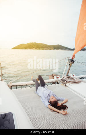 Jeune femme se reposant sur le pont du navire tout en profitant d'une croisière sur un bateau au coucher du soleil Banque D'Images