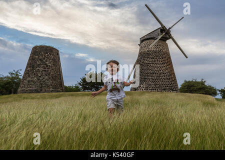 Enfant fonctionne sur de vertes prairies avec des moulins sur le contexte, Betty's Hope, antigua Banque D'Images