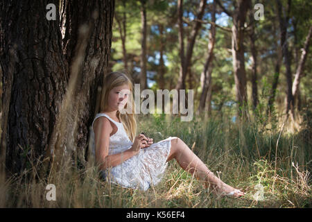 La fille aux cheveux longs en robe blanche, assis le dos appuyé contre l'arbre avec cône de pin dans les mains. fairy se ressemblent.