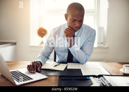 Les jeunes hommes et la lecture de documents et de travail sur un ordinateur portable tout en étant assis à son bureau dans un bureau Banque D'Images
