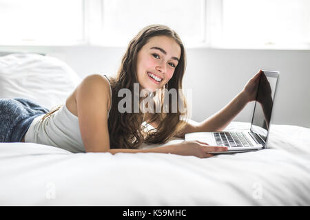 Teenage girl lying on bed using a laptop Banque D'Images