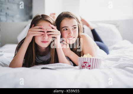 Teenage Girls eating popcorn et regarder des films d'horreur à la télé à la maison Banque D'Images