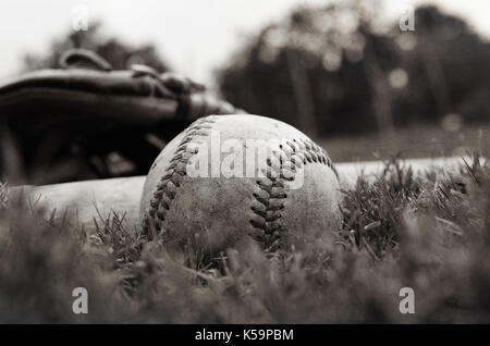 Old vintage baseball sur l'herbe après le jeu avec un gant et bat en arrière-plan. Banque D'Images