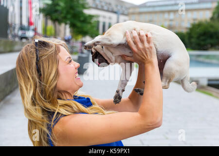 Jeune femme s'amuse en soulevant son mignon et pug Banque D'Images