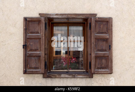 Vieille fenêtre en bois avec volets en bois naturel ouverte dans un mur de plâtre rugueux à la crème avec des reflets sur les vitres Banque D'Images