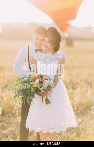 Marié est souriant serrant le vintage habillé avec la mariée bouquet énorme de retour à l'arrière-plan de la zone ensoleillée. Banque D'Images