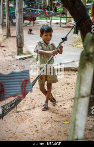 Siem Reap, Cambodge - 9/12/2015 : un jeune garçon joue avec un hamac en face de son village à la maison. Banque D'Images