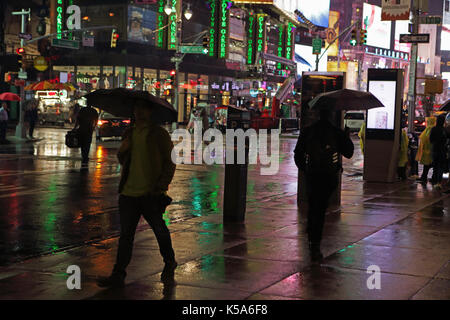 Rainy night in Times Square, les touristes avec des parasols à pied la 7ème avenue et Broadway vivement éclairée par les écrans des panneaux publicitaires électriques Banque D'Images