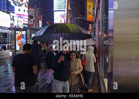 Rainy night in Times Square, les touristes avec des parasols à pied la 7ème avenue et Broadway vivement éclairée par les écrans des panneaux publicitaires électriques Banque D'Images