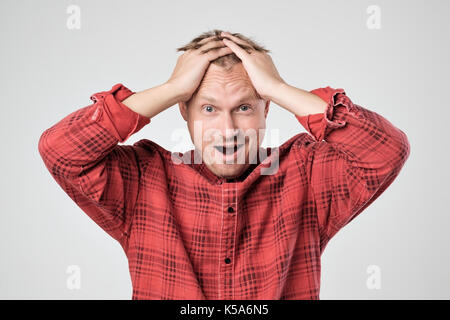 Portrait of young caucasian man in red t-shirt avec l'expression du visage choqué, isolé sur fond blanc Banque D'Images
