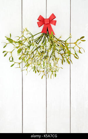 Bouquet de gui avec arc rouge sur fond de bois blanc en détresse. Banque D'Images