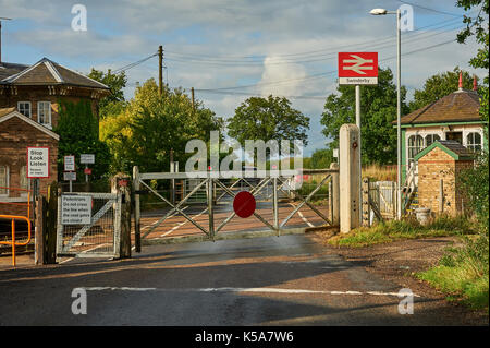 Les trains et les barrières du passage à niveau à commande manuelle dans le petit village de Rungis Lincolnshire Banque D'Images