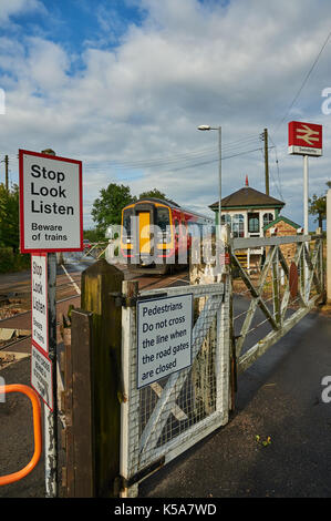 Les trains et les barrières du passage à niveau à commande manuelle dans le petit village de Rungis Lincolnshire Banque D'Images