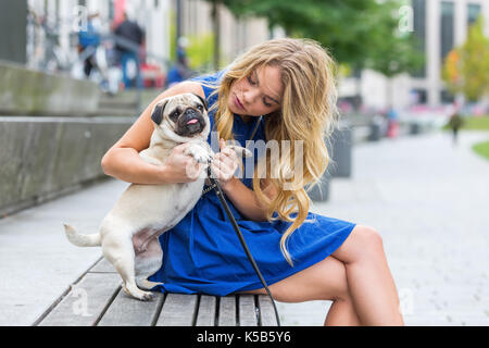 Jolie jeune femme joue avec son Carlin, sur un banc dans la ville Banque D'Images