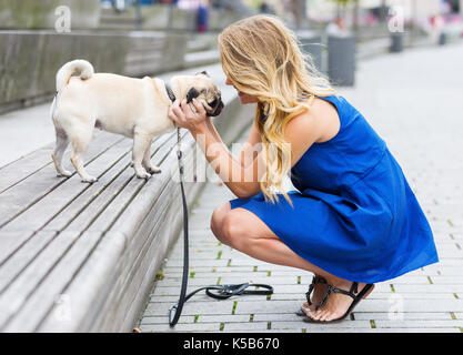 Jeune femme se caresse un carlin qui est assis sur un banc Banque D'Images