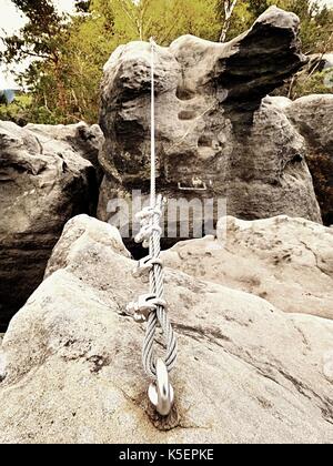 La corde tordue de fer tendus entre des roches dans les grimpeurs patch via ferrata. corde fixée en bloc par vis mousquetons. détail de l'extrémité de la corde ancrée dans l'al. Banque D'Images