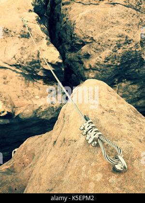 La corde tordue de fer tendus entre des roches dans les grimpeurs patch via ferrata. corde fixée en bloc par vis mousquetons. détail de l'extrémité de la corde ancrée dans l'al. Banque D'Images