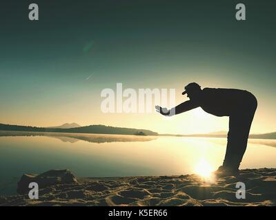 La respiration profonde runner silhouette pliée avec les mains sur les genoux. Vue de côté pour sports active man stretching muscles et exercer en mer plage. Bien réfléchir Banque D'Images