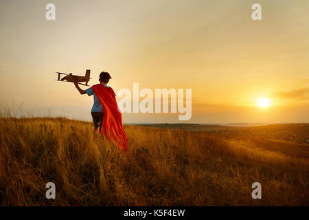 Un garçon en costume de marche pilote sur le terrain au coucher du soleil. Banque D'Images