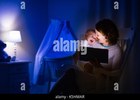 La mère et l'enfant de lire un livre dans une chambre sombre. maman et enfant à lire les livres avant de le mettre au lit. famille dans la soirée. chambre d'enfant intérieur avec une lampe de nuit Banque D'Images