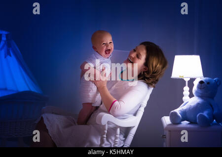 La mère et l'enfant de lire un livre dans une chambre sombre. maman et enfant à lire les livres avant de le mettre au lit. famille dans la soirée. chambre d'enfant intérieur avec une lampe de nuit Banque D'Images