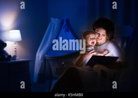 La mère et l'enfant de lire un livre dans une chambre sombre. maman et enfant à lire les livres avant de le mettre au lit. famille dans la soirée. chambre d'enfant intérieur avec une lampe de nuit Banque D'Images