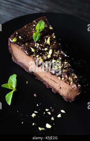 Gâteau au chocolat noir et pistaches hachées décoré de feuille de menthe sur la plaque noire sur la table en bois. Vue rapprochée Banque D'Images