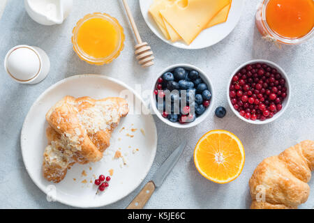 Le petit déjeuner continental en vue de dessus de table. des croissants frais, œuf dur, fromage, confiture, miel, orange, les bleuets et les raisins de table bleu horizon. Banque D'Images