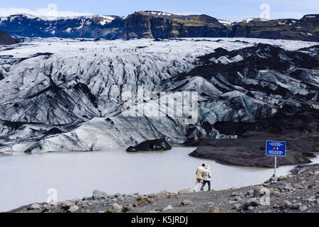 Un couple se promène devant le glacier Sólheimajökull dans le sud de l’Islande. Banque D'Images