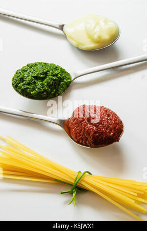 Spaghettis et trois cuillères avec différents condiments - sauce tomate, la mayonnaise et le pesto Banque D'Images