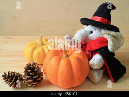 Poupée éléphant en costume de l'assistant d'une paire de couleurs vives venu citrouilles et deux cônes de pin on wooden table Banque D'Images