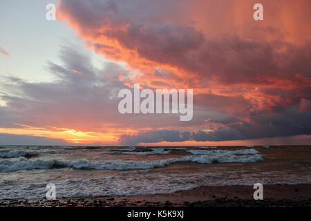 Une belle orange et rose coucher de soleil sur une plage sur le grand, wavey le lac Ontario. Banque D'Images