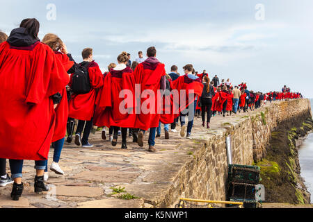 Freshers week à l'Université St Andrews, Fife, Royaume-Uni. Les élèves de leurs robes rouges brave le temps pour faire leur traditionnelle promenade le dimanche matin le long de la jetée. Banque D'Images