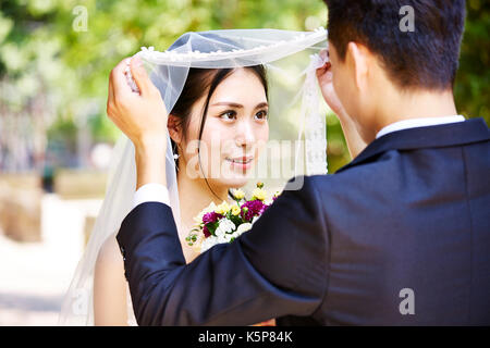 Asian groom soulevant Bridal Veil à baiser belle mariée. Banque D'Images