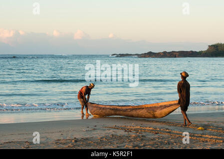 Les pêcheurs poussant un bateau à la mer au lever du soleil, la baie de Sainte Luce, Madagascar Banque D'Images