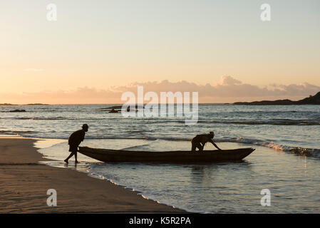 Les pêcheurs poussant un bateau à la mer au lever du soleil, la baie de Sainte Luce, Madagascar Banque D'Images