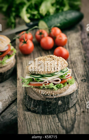 Délicieux jambon, fromage et salami sandwich avec des légumes, laitue, tomates cerise dans cadre naturel avec fond en bois Banque D'Images