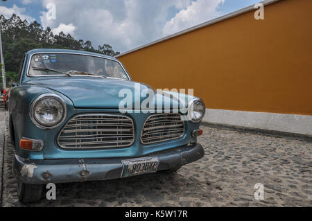 Une voiture bleue vintage avec une calandre distinctive garée sur une surface pavée sur un fond de mur jaune et un ciel nuageux. Banque D'Images