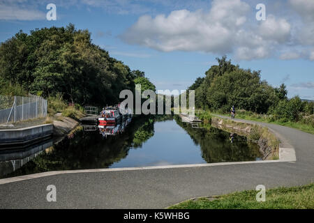 Bateau amarré à la jetée près de la roue de Falkirk Visitor's Center en tant que cyclistes passent par - sur les canaux écossais dans la région de Falkirk, Ecosse Banque D'Images