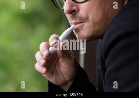 Caucasian man fumeurs de cigarette à l'extérieur de l'appareil hybride moderne Banque D'Images