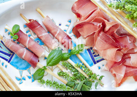 Plaque avec des bâtonnets enveloppés dans du prosciutto italien, décoré avec le basilic, vue du dessus. Banque D'Images