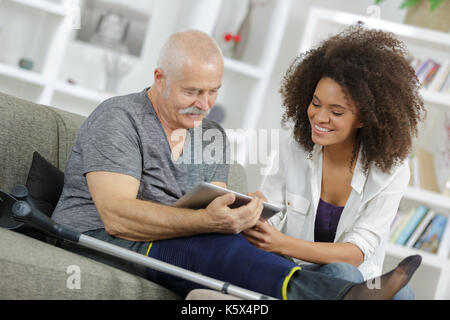 Jeune femme et homme senior chating avec la famille à l'aide de tablet Banque D'Images