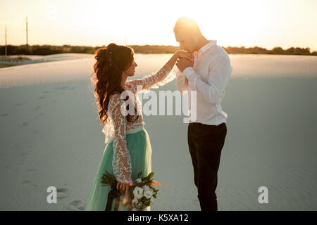 Le marié et la mariée embrasse la main dans desert au coucher du soleil. ils debout sur fond de sable blanc. close up. Banque D'Images