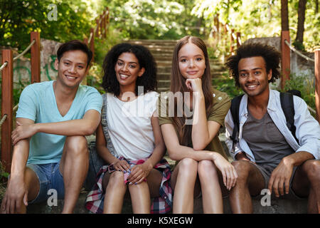 Quatre smiling friends sitting on stairs en forêt et regardant la caméra Banque D'Images